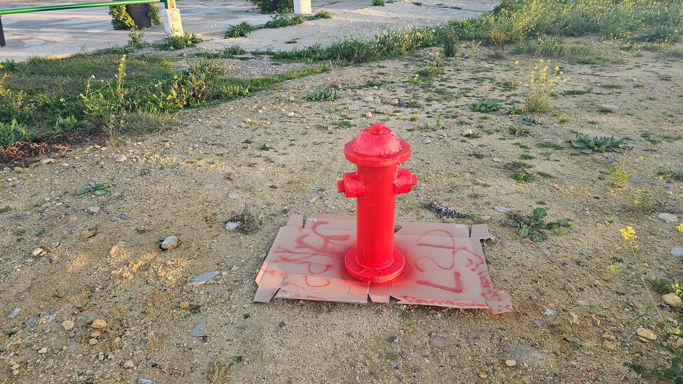 La boca de riego terminada, pintada de rojo, sobre el suelo a plena luz: de lejos pasa por hierro fundido.