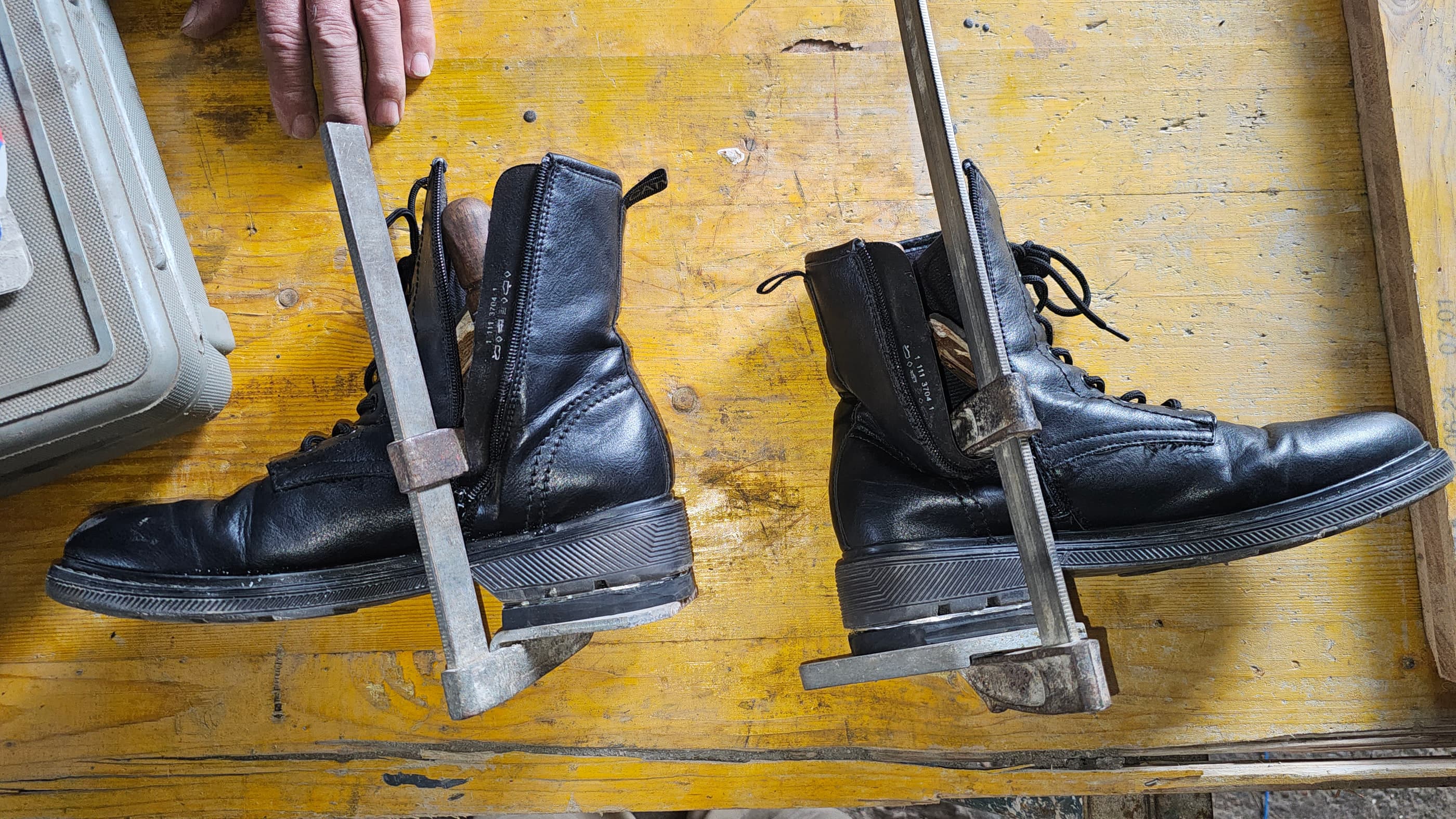 El par de botas negras sobre la mesa del taller, con la pieza de acero que asoma del talón y hace el truco.