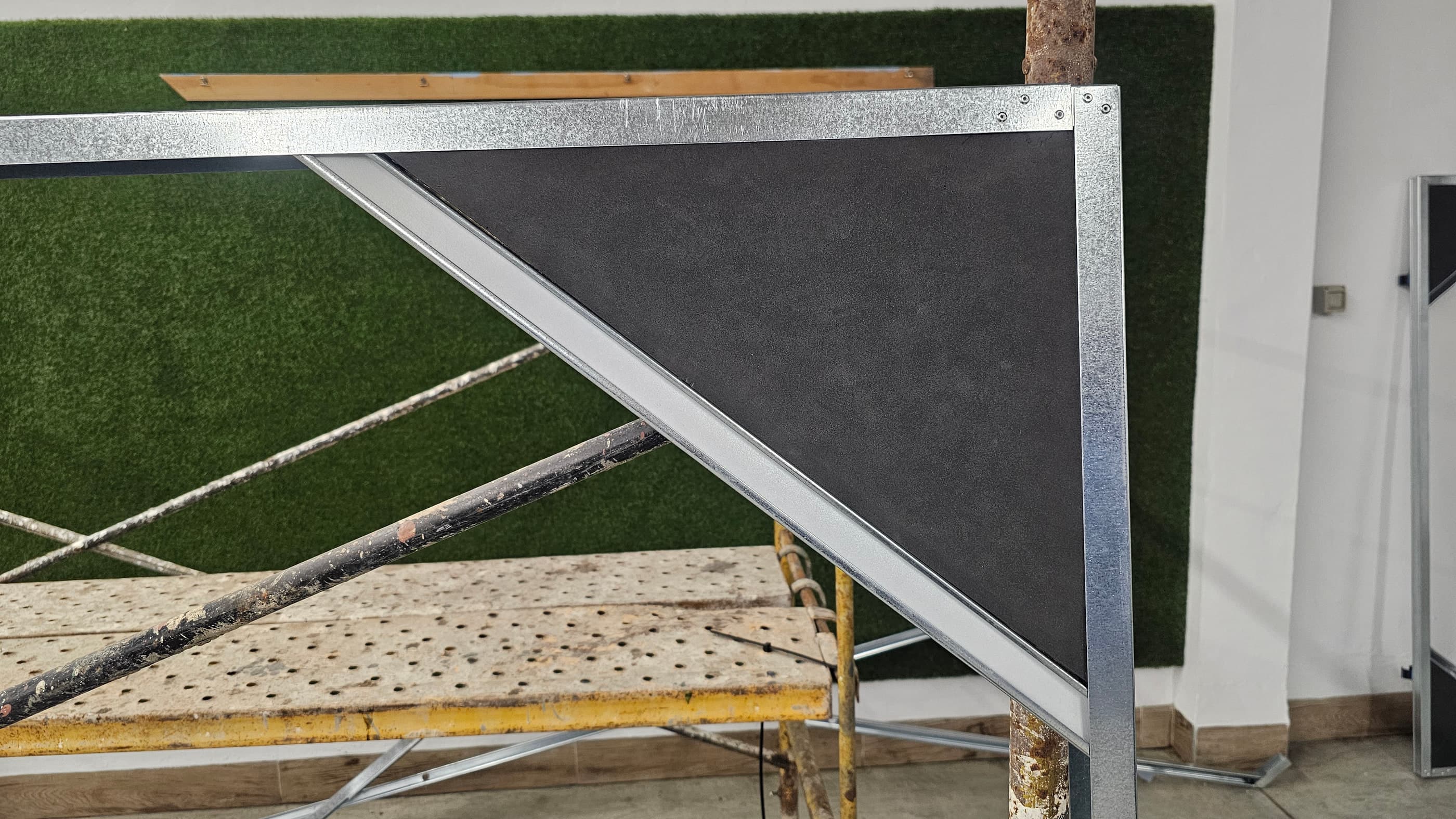Detalle de un panel: bastidor de acero galvanizado con el refuerzo diagonal y la superficie oscura.