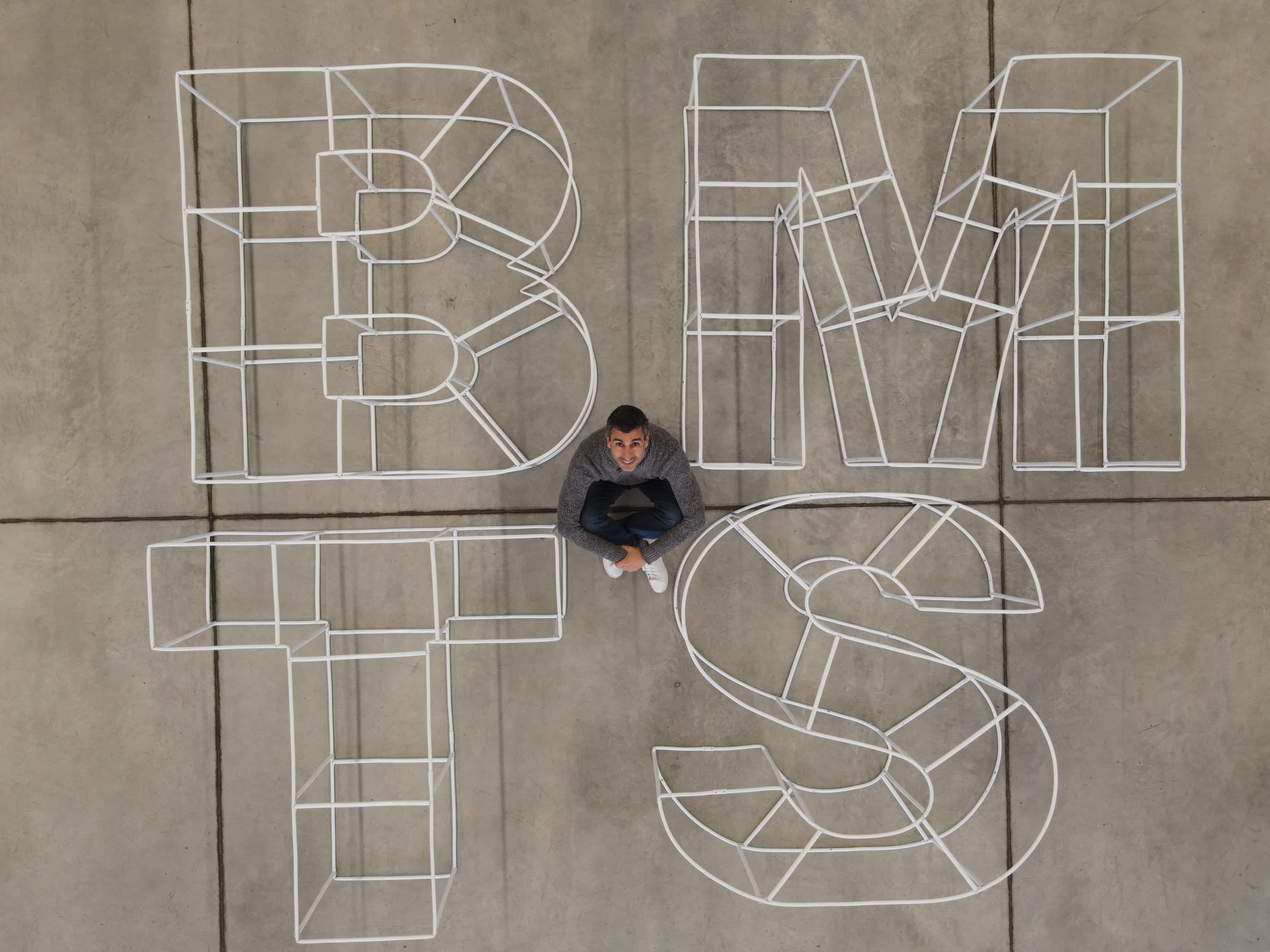 Las letras de tubo vistas desde un dron, dibujadas en volumen sobre un telón negro.