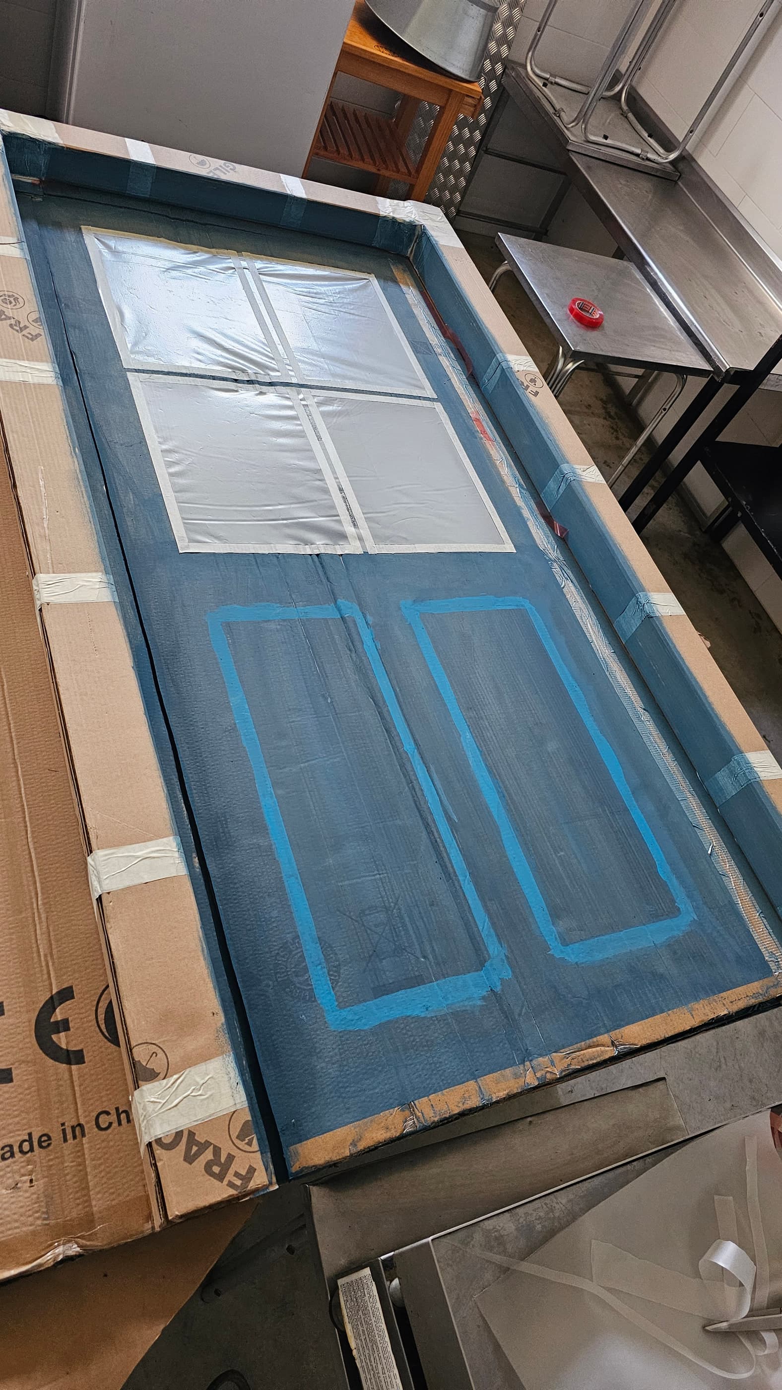 La puerta enmascarada con cinta durante el pintado, marcando los cuarterones y el ventanuco.