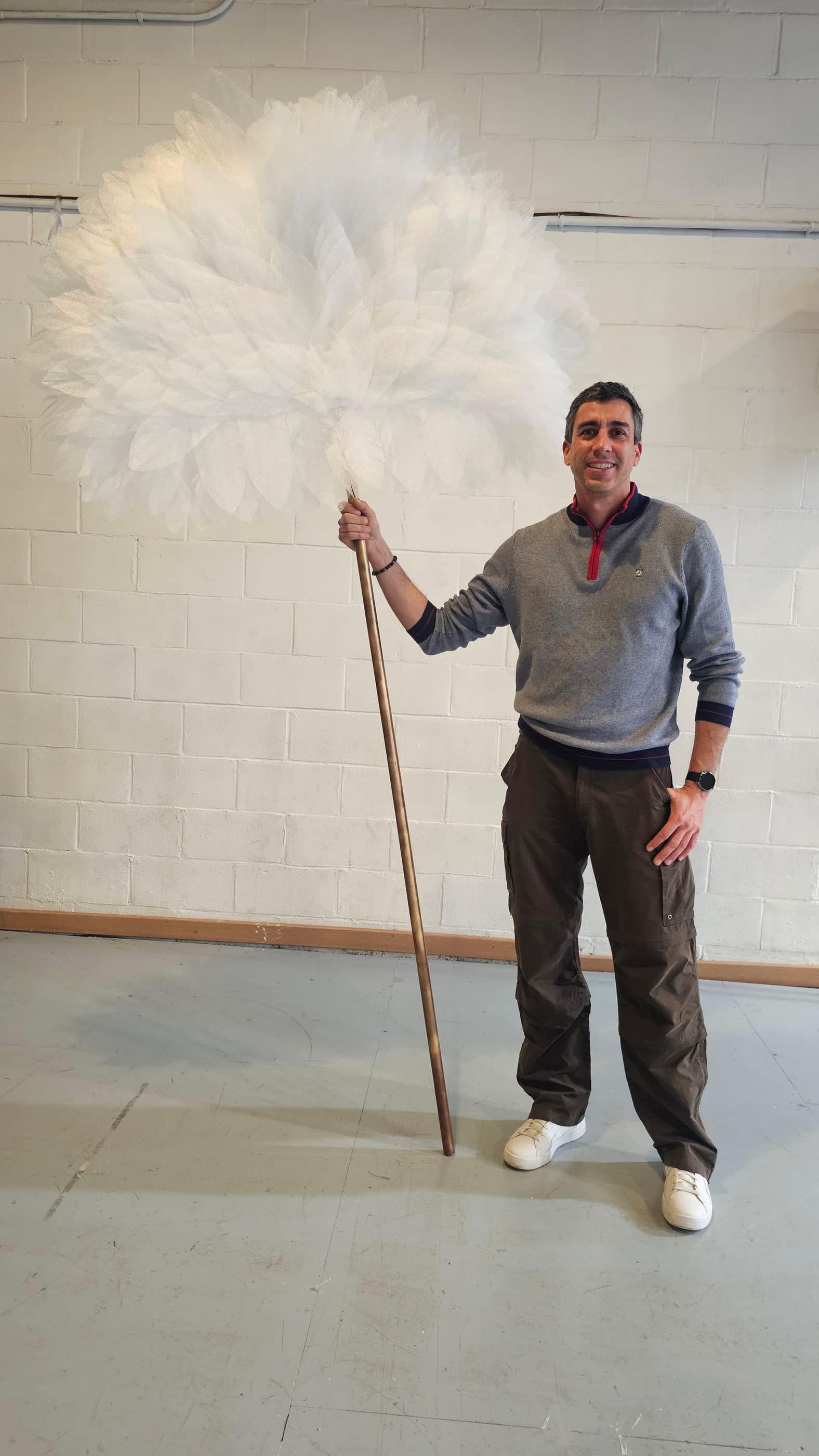 El abanico gigante de plumas de tul montado sobre una vara dorada; sostenido en pie, supera en altura a una persona.